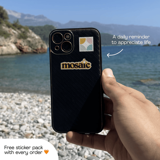 Phone with a Mosaic sticker held by the sea, a daily reminder to appreciate life